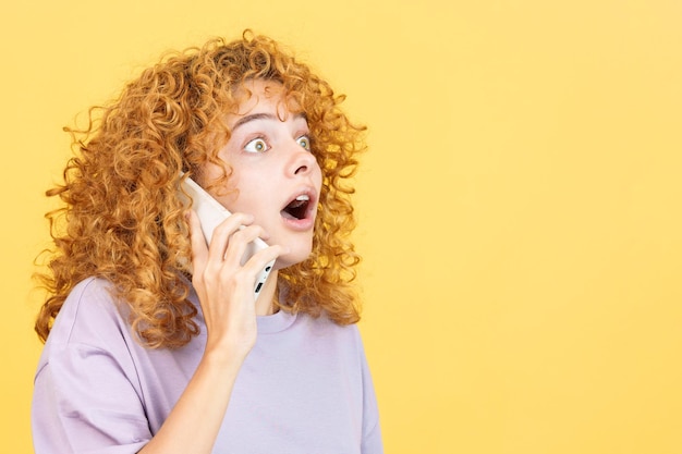 Удивленная женщина с вьющимися волосами разговаривает с мобильным телефоном