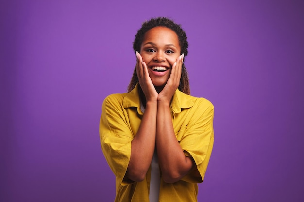 Surprised young African American woman with smile puts palms to cheeks