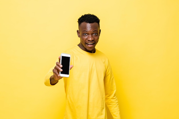 Surprised young African man showing mobile phone in his hand on yellow isolated studio background