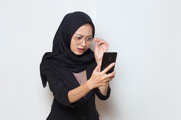 Surprised young asia muslim woman with glasses using mobile phone on white background