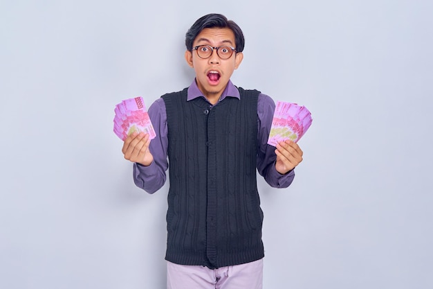 Surprised young Asian businessman Showing cash money in rupiah banknotes isolated on white background People lifestyle concept