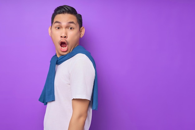 Surprised young Asian man wearing white tshirt is standing and looking at camera isolated over purple background people lifestyle concept