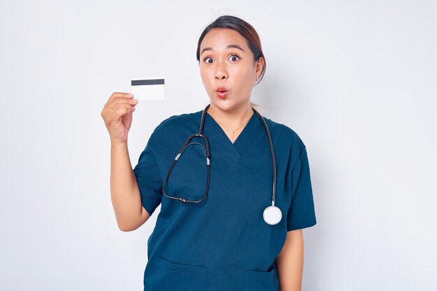 Surprised young Asian woman professional nurse working wearing blue uniform holding credit bank card isolated on white background Healthcare medicine concept