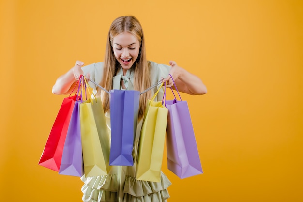 Surprised young beautiful girl with colorful shopping bags isolated over yellow