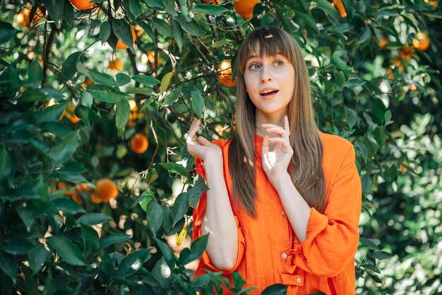 Surprised young girl in orange dress is thinking by looking up in orange garden