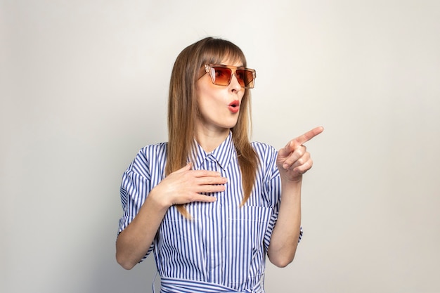 Surprised young girl shows a finger on a light background