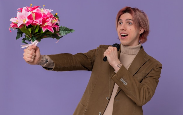 Surprised young handsome man holding bouquet of flowers and mic looking at side 