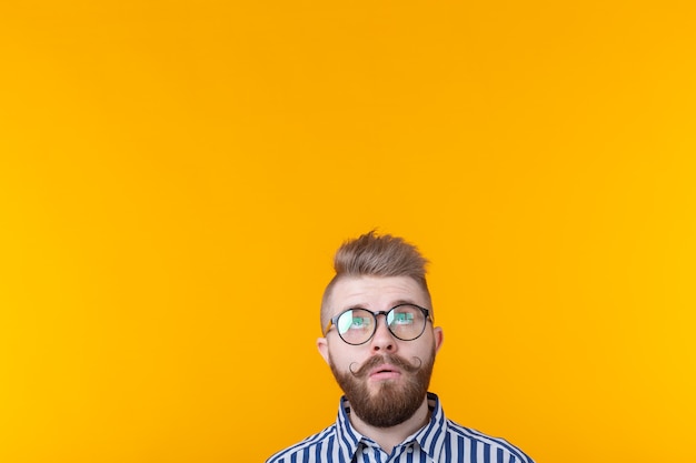 Surprised young hipster man with a mustache and with glasses posing on a yellow wall in