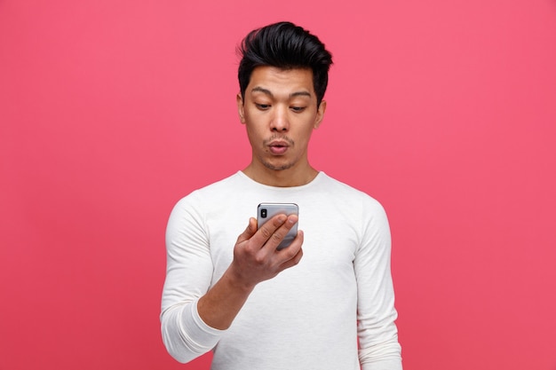 Surprised young man holding and looking at mobile phone 