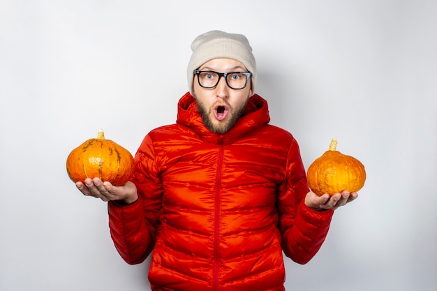 Surprised young man in a red jacket and hat, holds two pumpkins