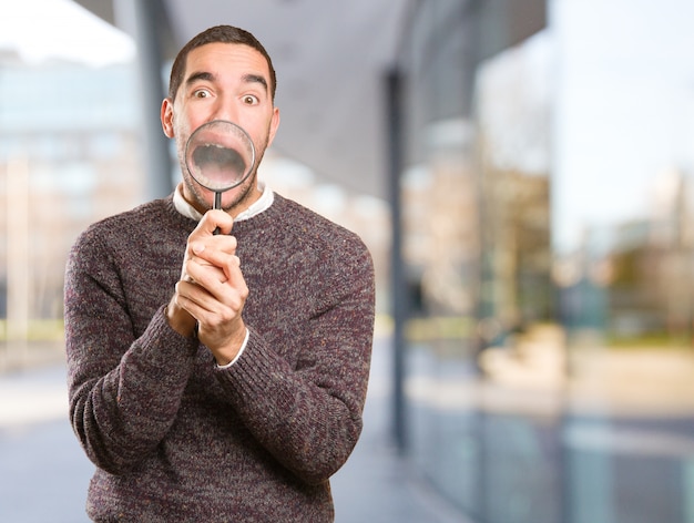 Surprised young man using a magnifying glass