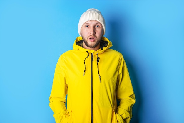 Surprised young man in a yellow jacket with a white hat on a blue background