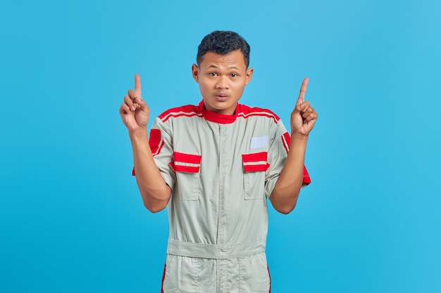 Surprised young mechanic while raised finger up isolated on blue background