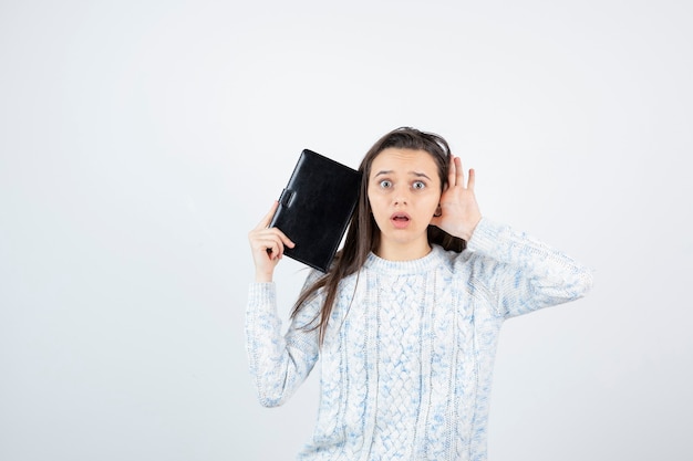 surprised young student posing with notebook on white wall.