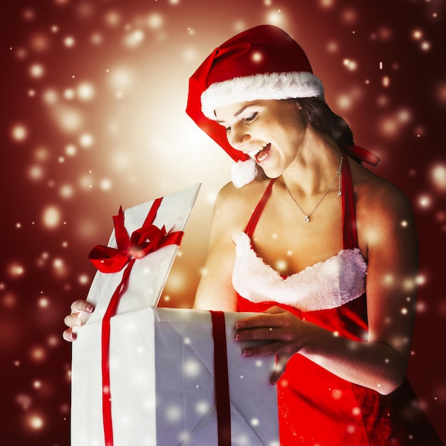 Surprised young woman in costume of Santa Claus opening a Christmas gift