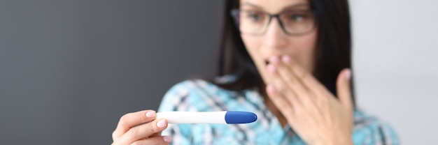 Surprised young woman covering her mouth with hand and looking at test at home. Pregnancy diagnosis test concept