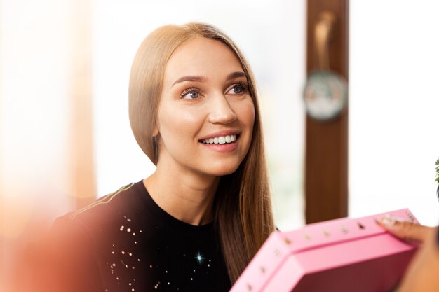 Surprised young woman opens a pink box with a present