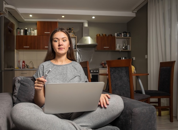 Foto giovane donna sorpresa e test di gravidanza con il laptop, donna alla ricerca di informazioni sulla gravidanza su internet con il laptop