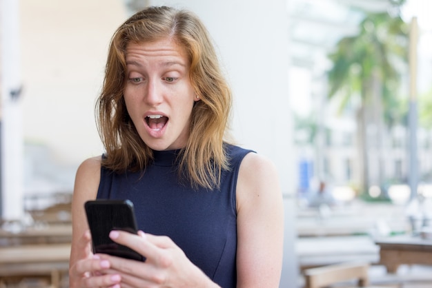 Surprised Young Woman Using Smartphone Outdoors