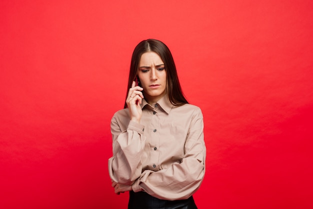 Surprised young woman using smartphone on red background