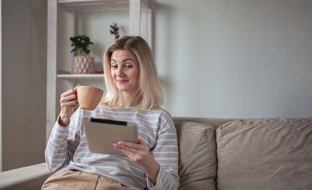 Surprised Young woman using tablet, sitting on sofa at home, dri