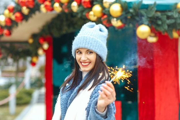 Surprised young woman wears blue coat enjoying holidays with bengal lights