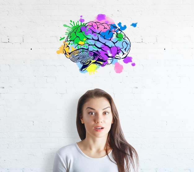 Surprised young woman on white brick background with colorful brain sketch Creative mind concept