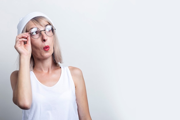 Surprised young woman in a white hat and glasses on a light background.