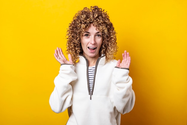 Surprised young woman with curly African hair on a yellow background.