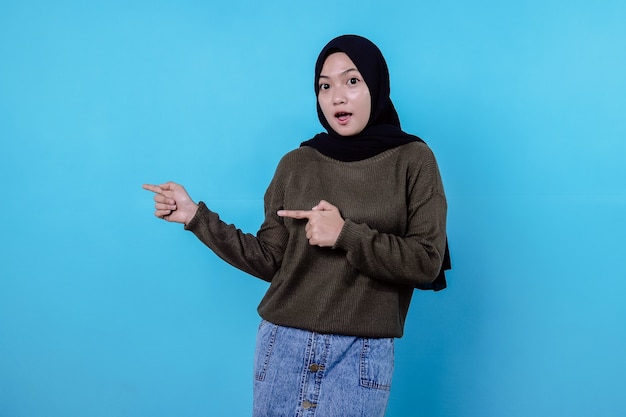 Surprising happy asian woman with her finger pointing isolated on light blue banner background