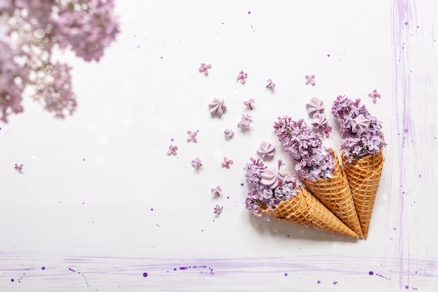 Photo surreal lilac flowers and meringue cookies in waffle cones on white background with watercolor patternx9