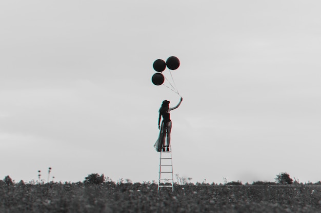 Surreal photo of a lonely girl on the stairs with balloons. the concept of freedom and independence. black and white with 3d glitch virtual reality effect