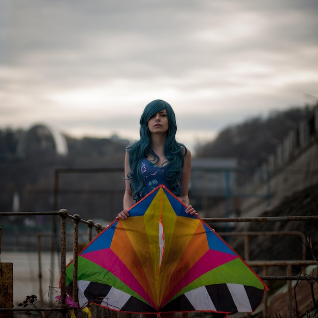 Surreal photography. Portrait of a girl with blue hair on the waterfront with a kite in her hands.