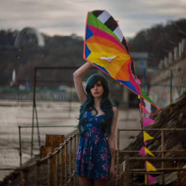 Surreal photography. Portrait of a girl with blue hair on the waterfront with a kite in her hands.