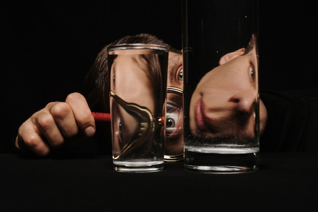 Surrealistisch portret van een man die door een vergrootglas en glazen water kijkt