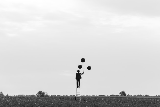 Surrealistisch silhouet van een man in een pak die op de trap in een veld met ballonnen staat. Concept van vrijheid