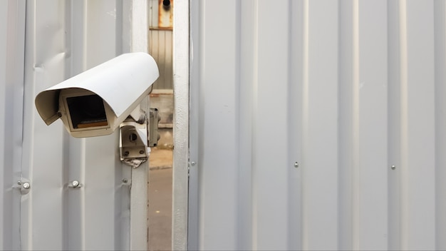 Surveillance camera on top of a gray corrugated metal fence.
