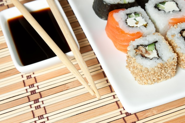 Sushi assortment on white plate, with soy sauce over bamboo background.