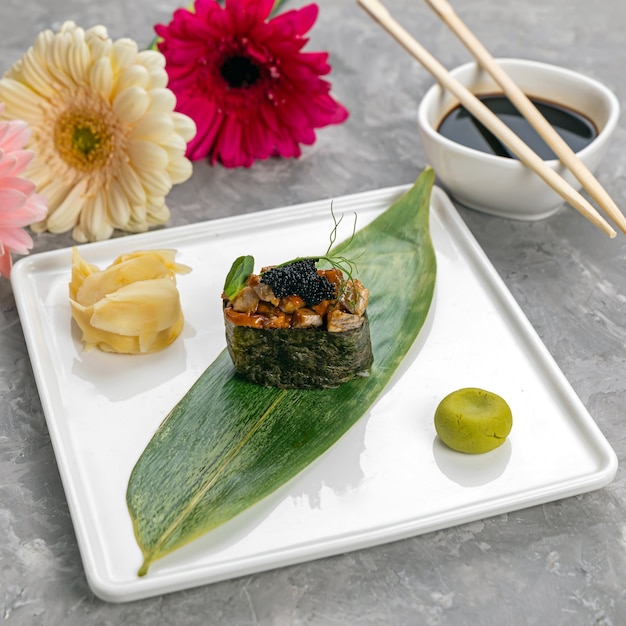 Sushi on a banana leaf with sauce on a white plate