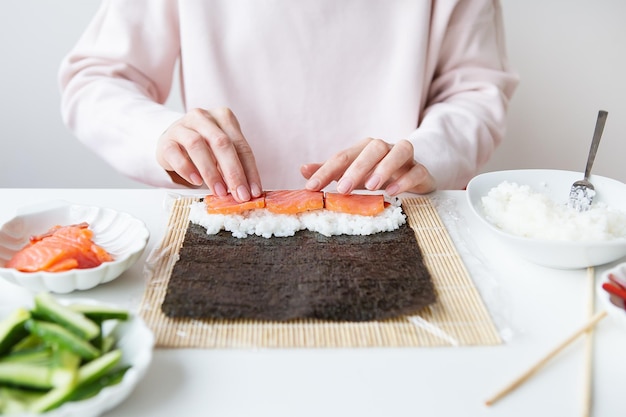 Sushi bereidingsproces, het meisje maakt sushi met verschillende smaken - verse zalm, kaviaar, avocado, komkommer, gember, rijst.