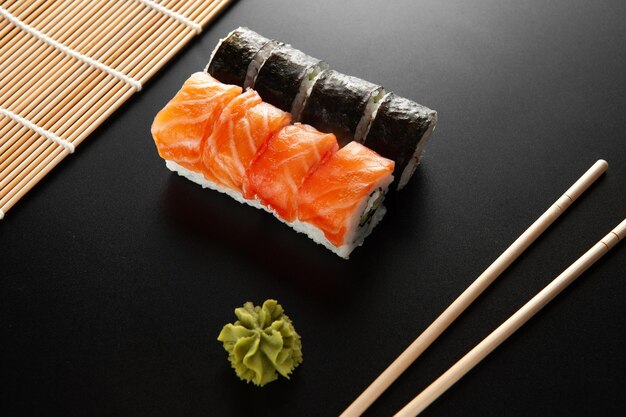 Sushi on a black background sushi california alongside bamboo\
sticks and wasabi