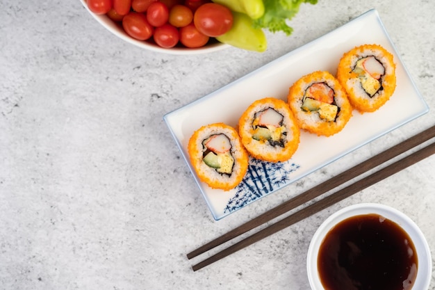 Photo sushi is in a plate with chopsticks and dipping sauce on a white cement floor