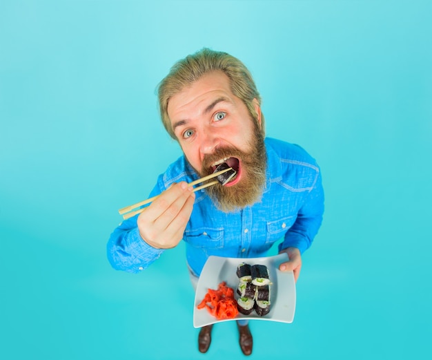 Photo sushi. japan. sushi delivery. japanese food. bearded man with plate of sushiroll. man eating sushi. man with sushi on chopstick. pickled ginger. plate of rolls. susi. exotic nutrition.