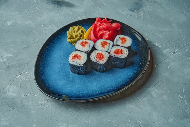 Foto sushi maki roll con salmone su un piatto blu su una superficie grigia. cucina giapponese