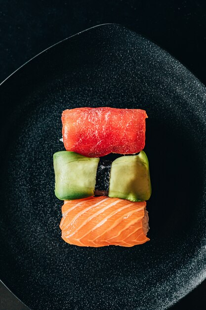 Foto sushi met avocado, tonijn en zalm op een zwarte plaat