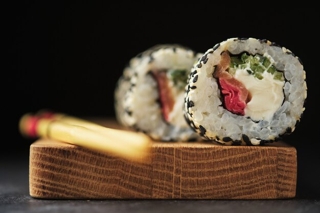 Sushi op een houten bord. Rollen met vis op een donkere achtergrond.