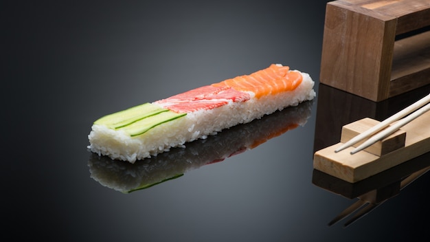 Sushi op zwarte achtergrond met stokjes. houten persvorm voor het maken van sushi