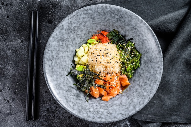 Sushi poke bowl met komkommer, zalm, avocado. Aziatisch trendy eten. Zwarte achtergrond. Bovenaanzicht. Kopieer ruimte.