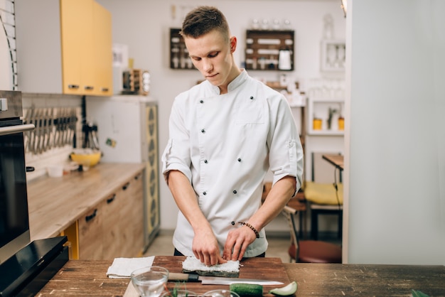 Sushi preparation, traditional japanese cuisine. Male cook making rolls on the kitchen