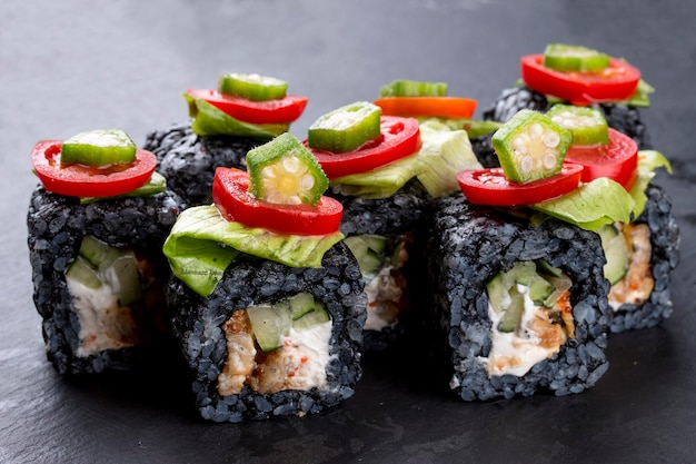 Sushi roll in black rice with eel and tomatoes on black background